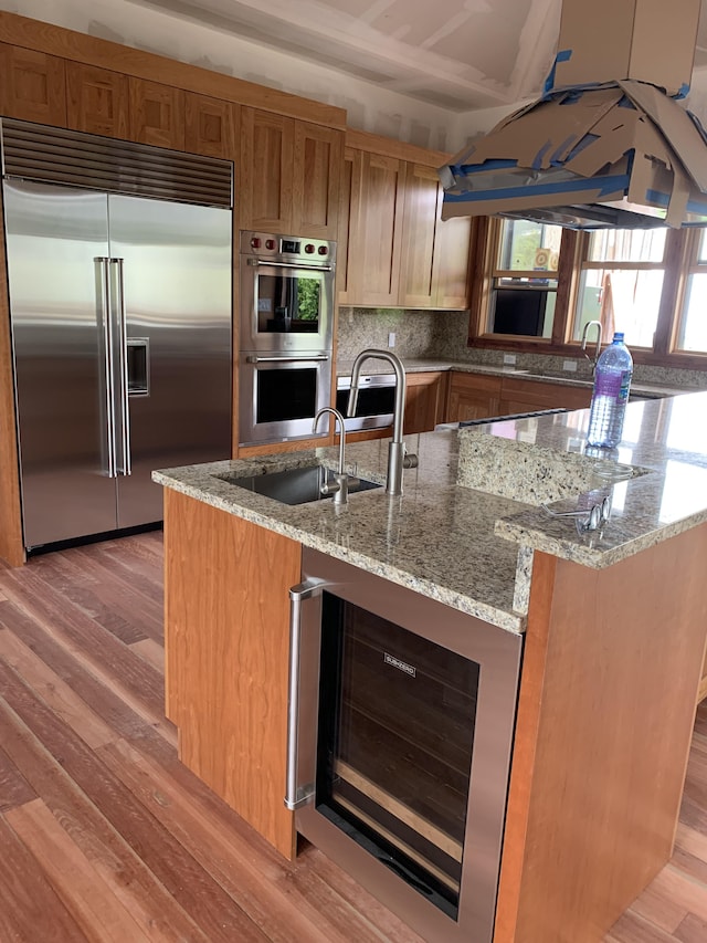 kitchen with stainless steel appliances, light hardwood / wood-style floors, wine cooler, and light stone countertops