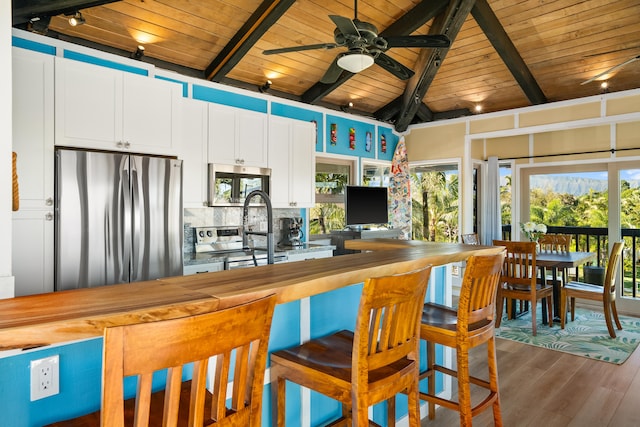 kitchen with white cabinets, butcher block countertops, beamed ceiling, stainless steel appliances, and backsplash