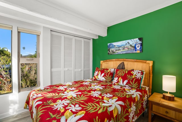 bedroom with a closet, beamed ceiling, and wood finished floors