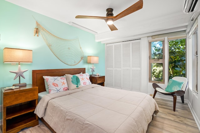 bedroom featuring baseboards, light wood-style flooring, ceiling fan, a wall mounted air conditioner, and a closet