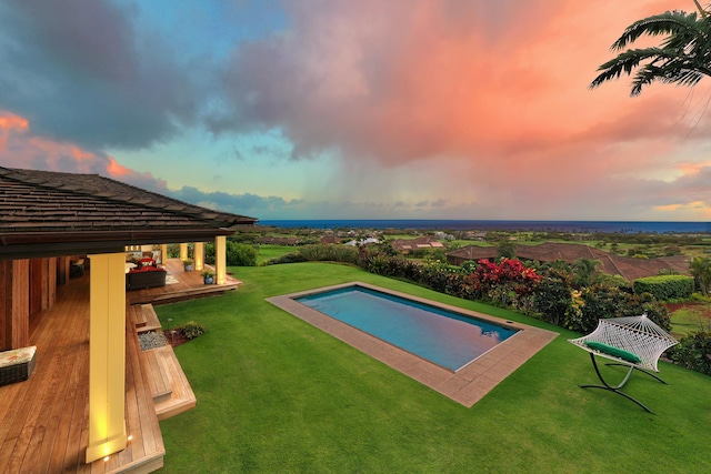 pool at dusk featuring a deck and a yard