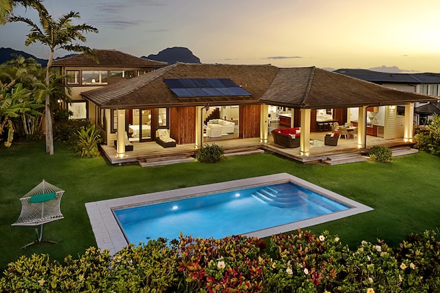 back house at dusk featuring an outdoor hangout area, a lawn, a swimming pool side deck, and solar panels