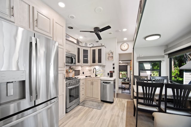 kitchen featuring appliances with stainless steel finishes, tasteful backsplash, sink, ceiling fan, and light hardwood / wood-style flooring