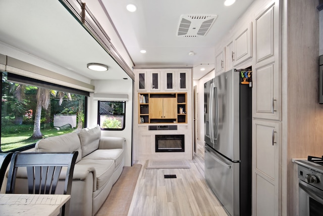 kitchen featuring white cabinetry, stainless steel fridge with ice dispenser, light wood-type flooring, and range