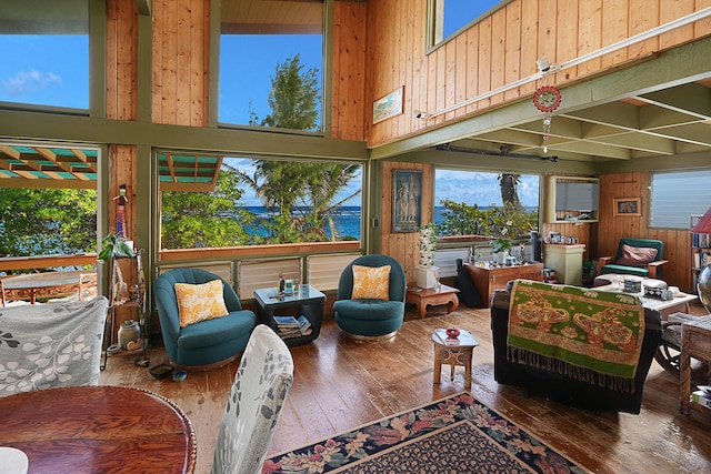 living room with hardwood / wood-style floors, a towering ceiling, wooden walls, and a water view