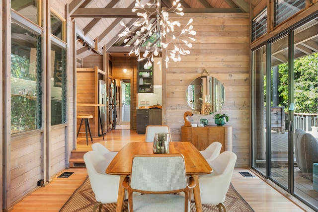 dining space with light hardwood / wood-style flooring, beam ceiling, wooden ceiling, an inviting chandelier, and wooden walls