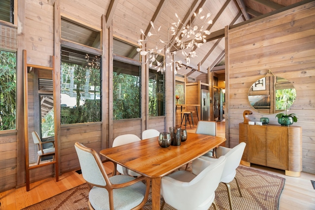 dining area featuring light wood-type flooring, wooden ceiling, vaulted ceiling with beams, wooden walls, and a chandelier