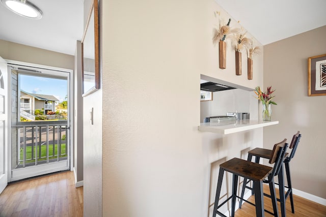 interior space featuring wall chimney exhaust hood, a kitchen breakfast bar, and light hardwood / wood-style flooring