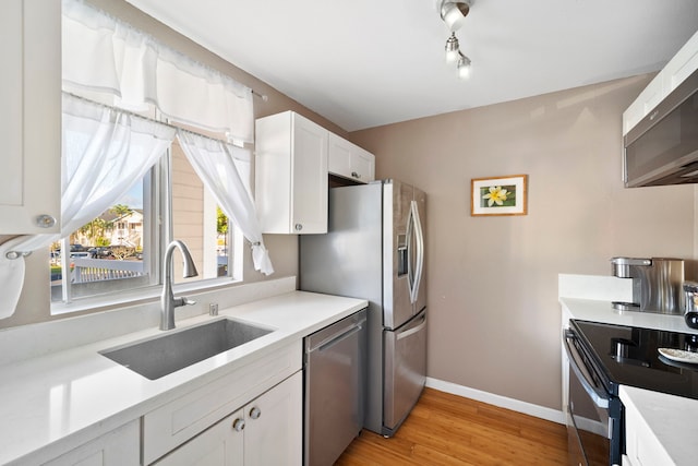 kitchen with sink, rail lighting, stainless steel appliances, light hardwood / wood-style floors, and white cabinets