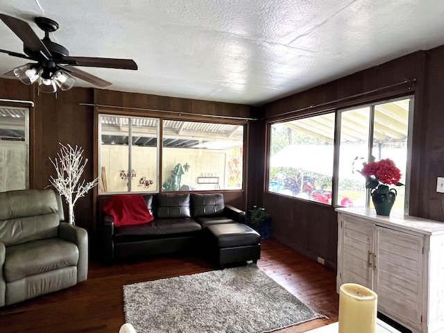 living room with ceiling fan, dark hardwood / wood-style floors, a textured ceiling, and wood walls