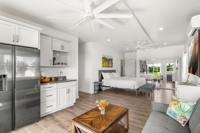 bedroom with an AC wall unit, stainless steel fridge, ceiling fan, light hardwood / wood-style floors, and wet bar