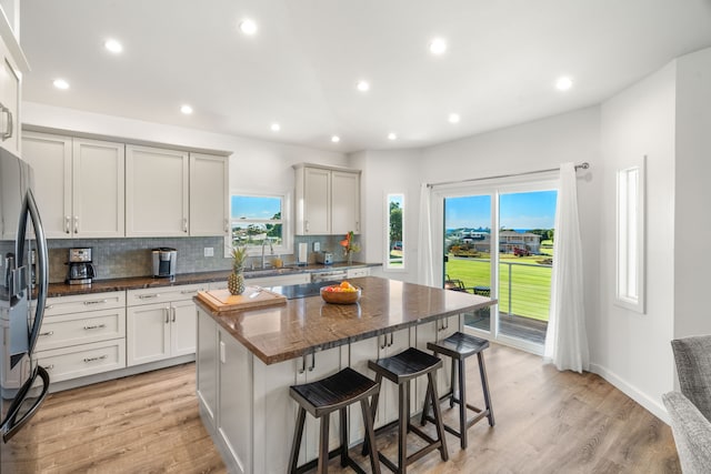 kitchen featuring light hardwood / wood-style flooring, dark stone countertops, stainless steel fridge, a kitchen island, and decorative backsplash