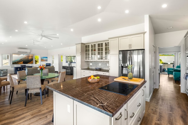 kitchen featuring stainless steel refrigerator with ice dispenser, white cabinetry, an AC wall unit, black electric cooktop, and a kitchen island