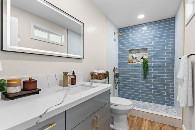 bathroom with hardwood / wood-style flooring, vanity, toilet, and a tile shower