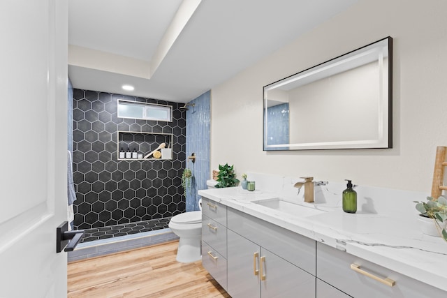 bathroom with wood-type flooring, tiled shower, vanity, and toilet