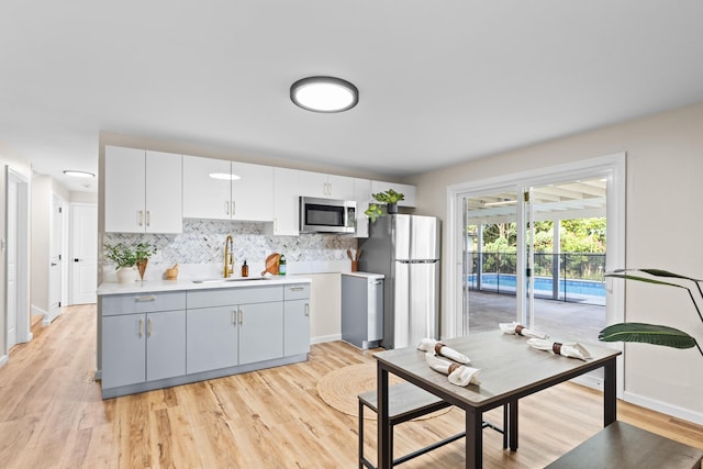 kitchen with appliances with stainless steel finishes, sink, white cabinets, backsplash, and light hardwood / wood-style floors