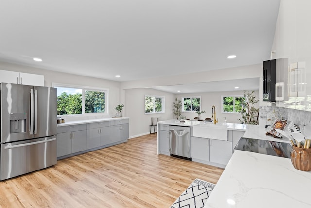 kitchen featuring gray cabinetry, light wood-type flooring, appliances with stainless steel finishes, light stone countertops, and white cabinets