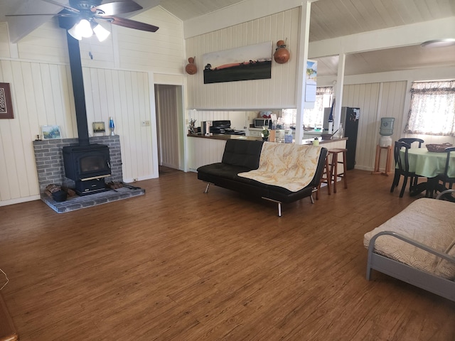 living room with ceiling fan, dark hardwood / wood-style floors, lofted ceiling with beams, and a wood stove