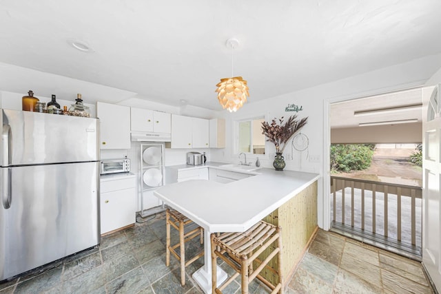 kitchen with a breakfast bar, decorative light fixtures, white cabinets, stainless steel fridge, and kitchen peninsula