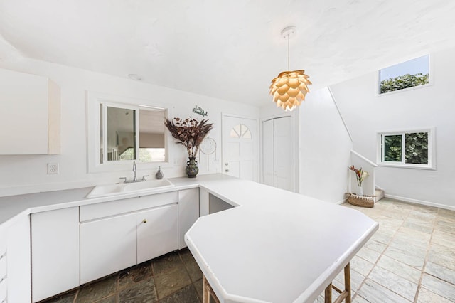 kitchen featuring hanging light fixtures, sink, white cabinets, and kitchen peninsula