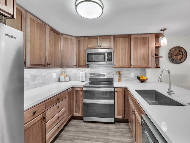 kitchen featuring sink, light wood-type flooring, pendant lighting, stainless steel appliances, and backsplash