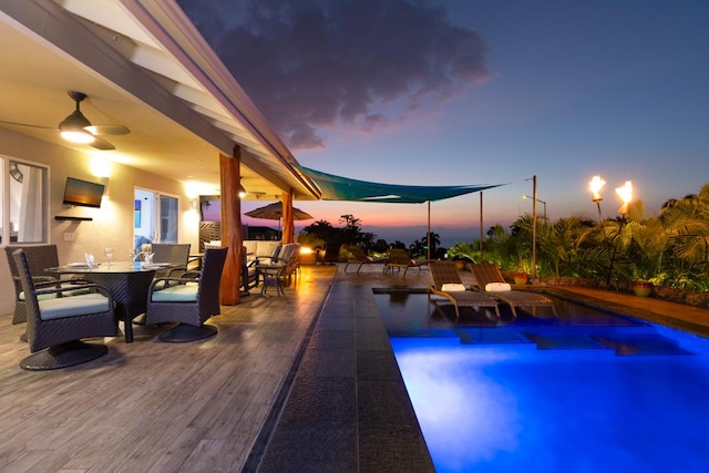 pool at dusk featuring outdoor dining area, ceiling fan, and an outdoor pool