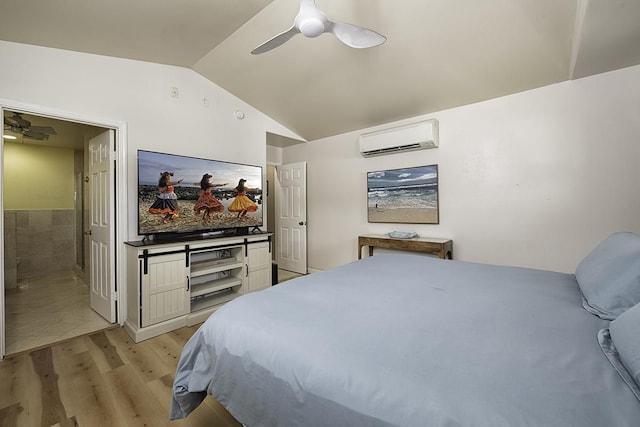 bedroom featuring vaulted ceiling, connected bathroom, a wall unit AC, ceiling fan, and light wood-type flooring