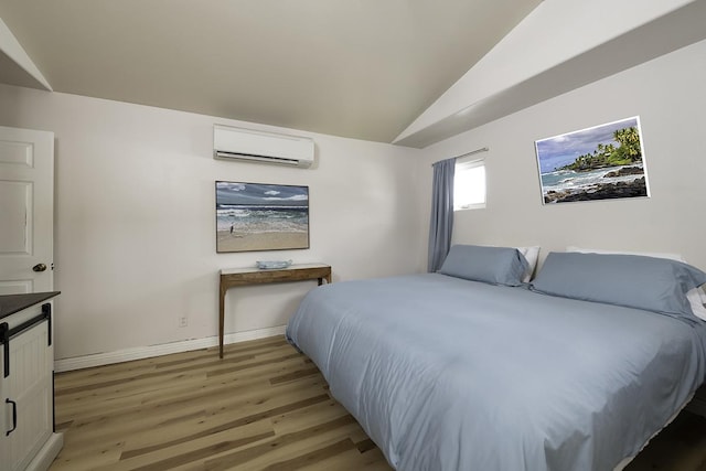 bedroom with vaulted ceiling, a wall unit AC, and light hardwood / wood-style floors