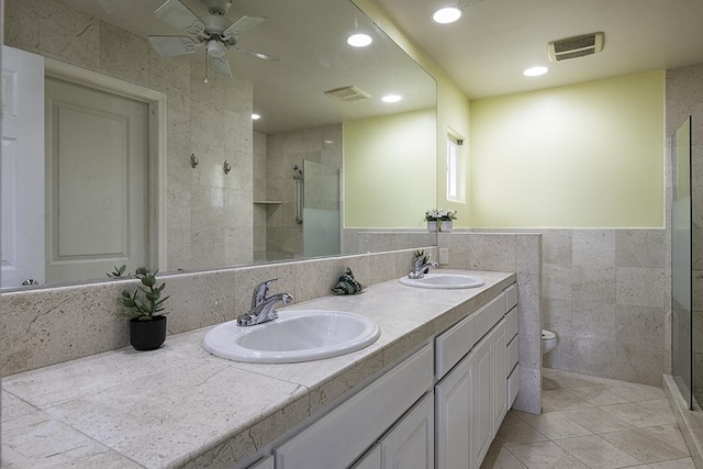 bathroom with tile walls, tiled shower, vanity, tile patterned floors, and toilet