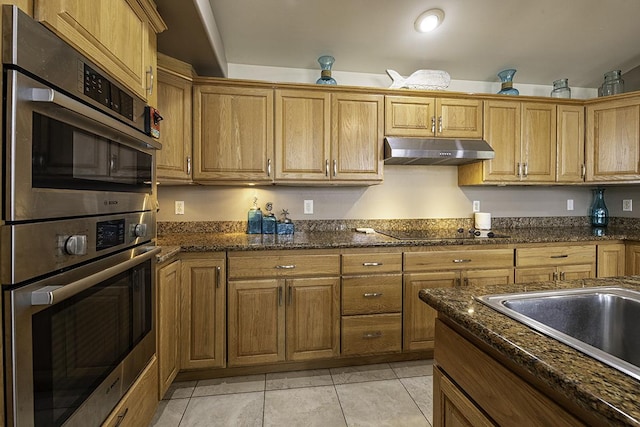 kitchen featuring double oven, sink, dark stone counters, light tile patterned floors, and black electric stovetop