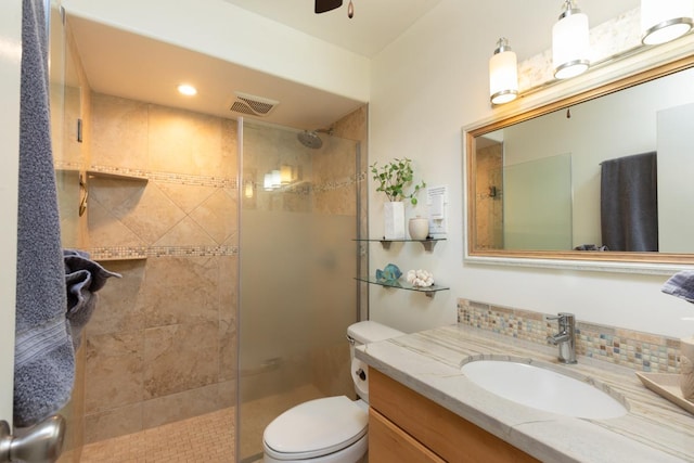 bathroom with toilet, tasteful backsplash, a tile shower, vanity, and ceiling fan