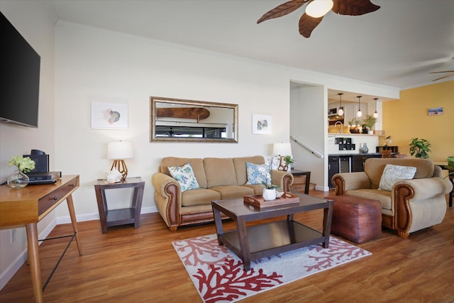 living room featuring ornamental molding, wood finished floors, baseboards, and a ceiling fan