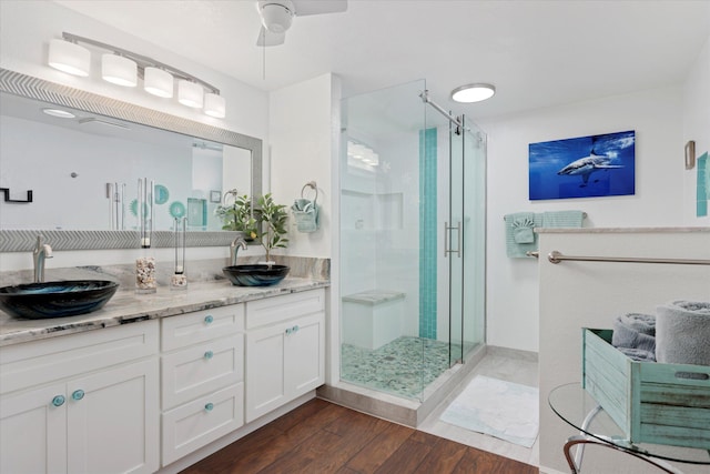 bathroom with double vanity, wood finished floors, a sink, and a shower stall