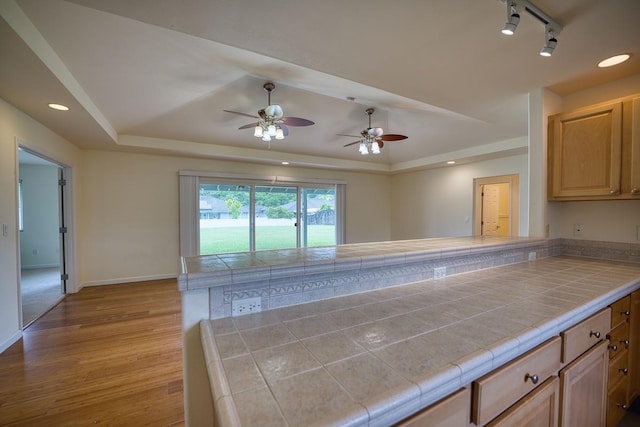 kitchen with tile countertops, light brown cabinetry, light wood-type flooring, and a tray ceiling