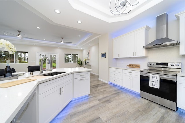 kitchen with stainless steel electric stove, dishwasher, white cabinetry, a tray ceiling, and wall chimney range hood