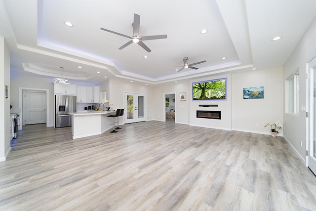 unfurnished living room featuring ceiling fan, sink, light hardwood / wood-style flooring, and a raised ceiling