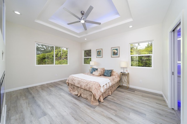 bedroom featuring ceiling fan, a tray ceiling, and light hardwood / wood-style flooring