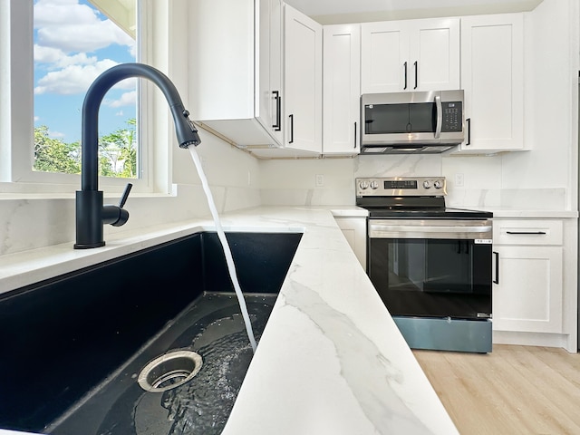 kitchen with light stone counters, sink, stainless steel appliances, and white cabinets