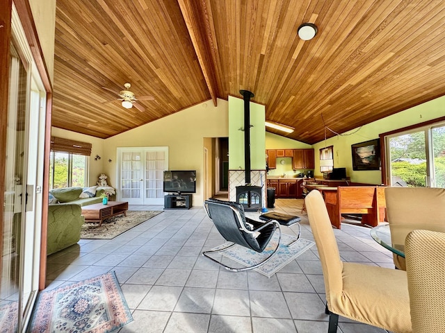 living room featuring lofted ceiling with beams, a wood stove, light tile patterned floors, ceiling fan, and wooden ceiling