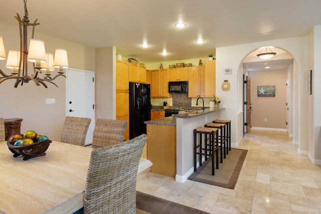 kitchen featuring sink, dark stone countertops, black appliances, decorative backsplash, and kitchen peninsula