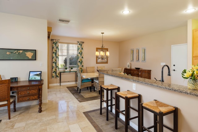 kitchen with a breakfast bar, sink, a chandelier, hanging light fixtures, and light stone counters