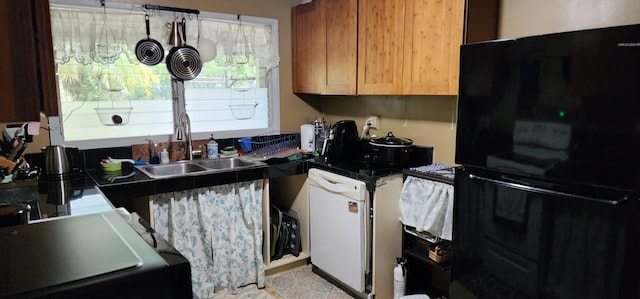 kitchen featuring freestanding refrigerator, a sink, dark countertops, dishwasher, and range
