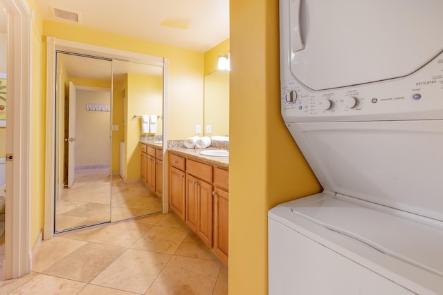 washroom with light tile patterned flooring, stacked washing maching and dryer, and sink