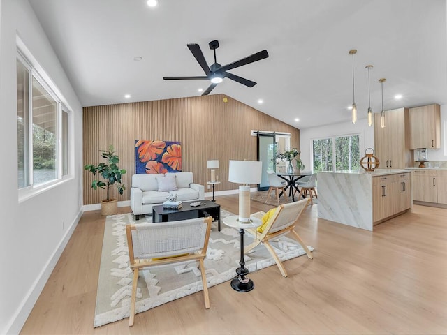 living room featuring wood walls, lofted ceiling, ceiling fan, a barn door, and light wood-type flooring