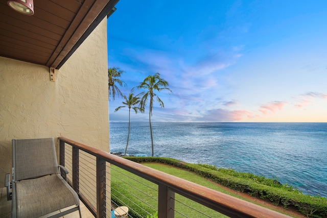 balcony at dusk featuring a water view