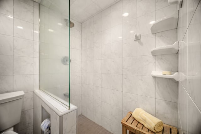 bathroom with tile walls, toilet, and tiled shower