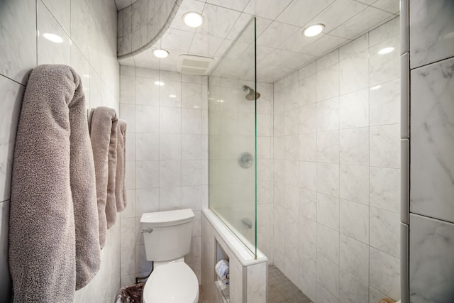 bathroom featuring a tile shower, tile walls, and toilet