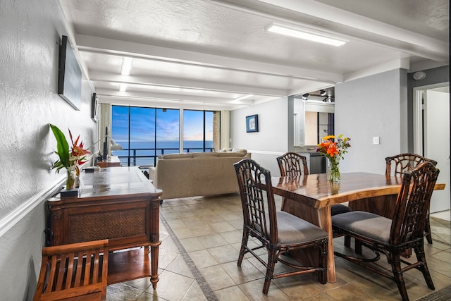 tiled dining space with beamed ceiling, a textured ceiling, and a water view