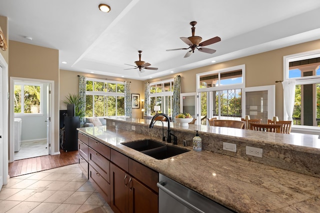 kitchen featuring sink, light tile patterned floors, a tray ceiling, dishwasher, and light stone countertops