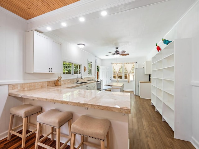 kitchen featuring sink, a breakfast bar area, stainless steel refrigerator, white cabinetry, and kitchen peninsula